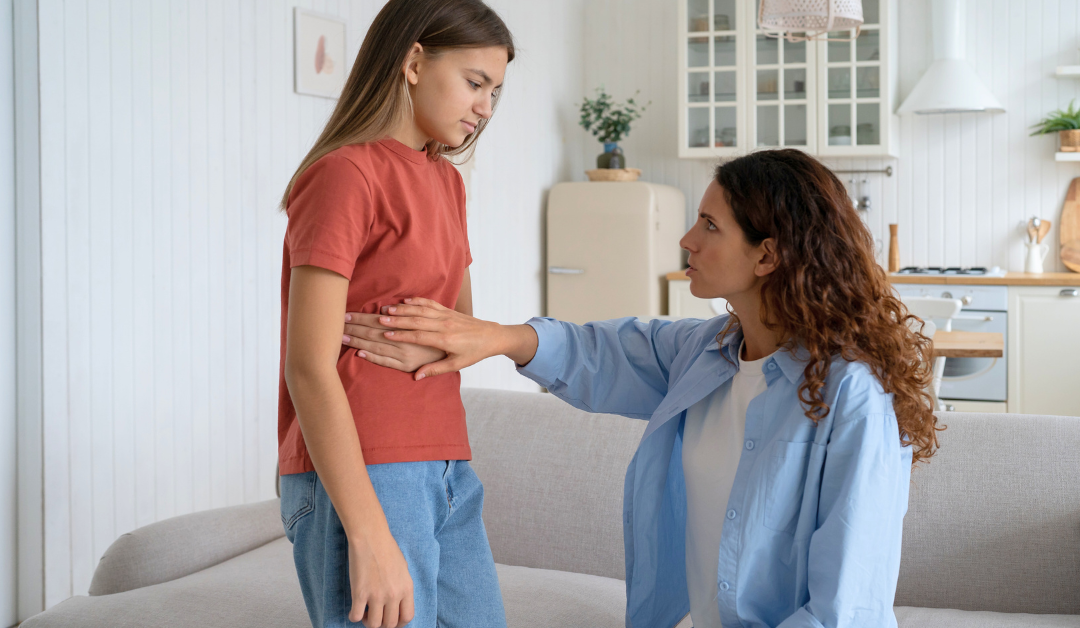 A mother holds her hand to her daughter's stomach who appears to have stomach pains